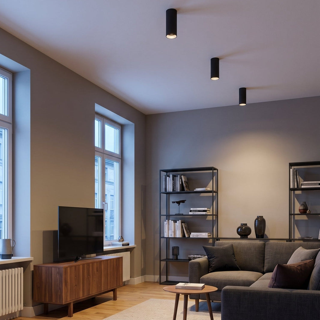 Salon aux murs gris avec trois spots tube Tubélis noirs en saillie au plafond, sans faux plafond