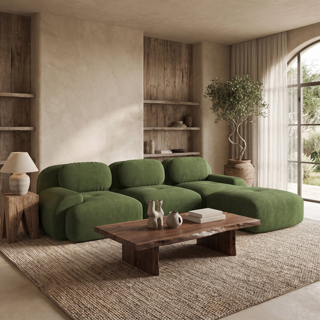 Canapé d'angle modulable en velours côtelé vert avec méridienne dans un salon naturel, devant une table basse en bois