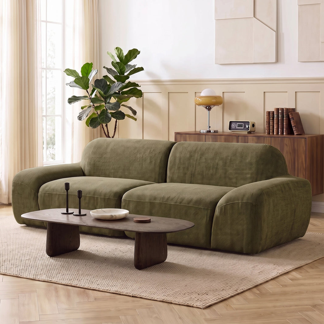Canapé 3 places en chenille vert olive aux volumes arrondis dans un salon clair, devant une table basse en bois foncé