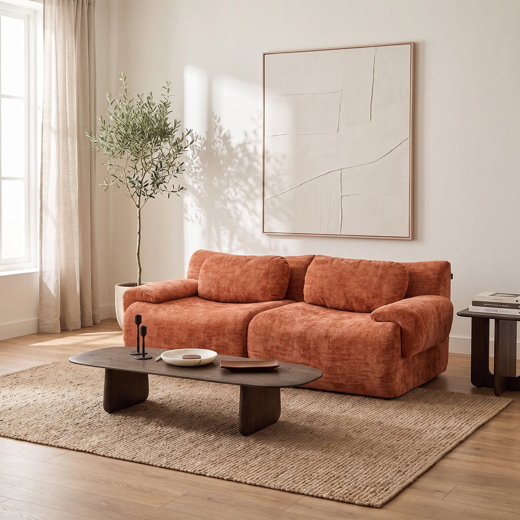Canapé-lit 2 places en chenille orange dans un petit salon clair, avec table basse ovale en bois foncé et tapis