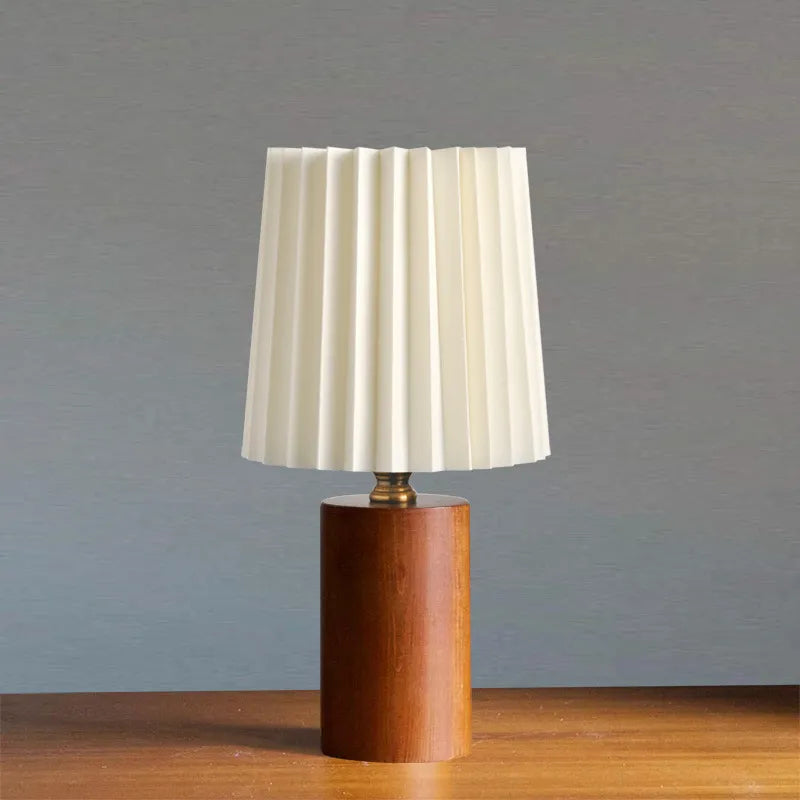 Lampe de table élégante au design intemporel avec une base cylindrique en bois naturel et un abat-jour plissé. Parfaite pour ajouter une touche sophistiquée et chaleureuse à une chambre, un salon ou un bureau.