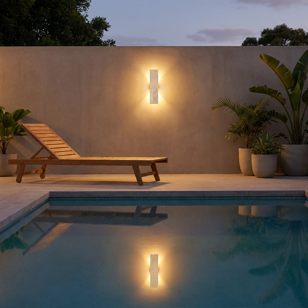 Applique extérieure en travertin Stélia sur un mur de terrasse au bord d'une piscine, reflet dans l'eau