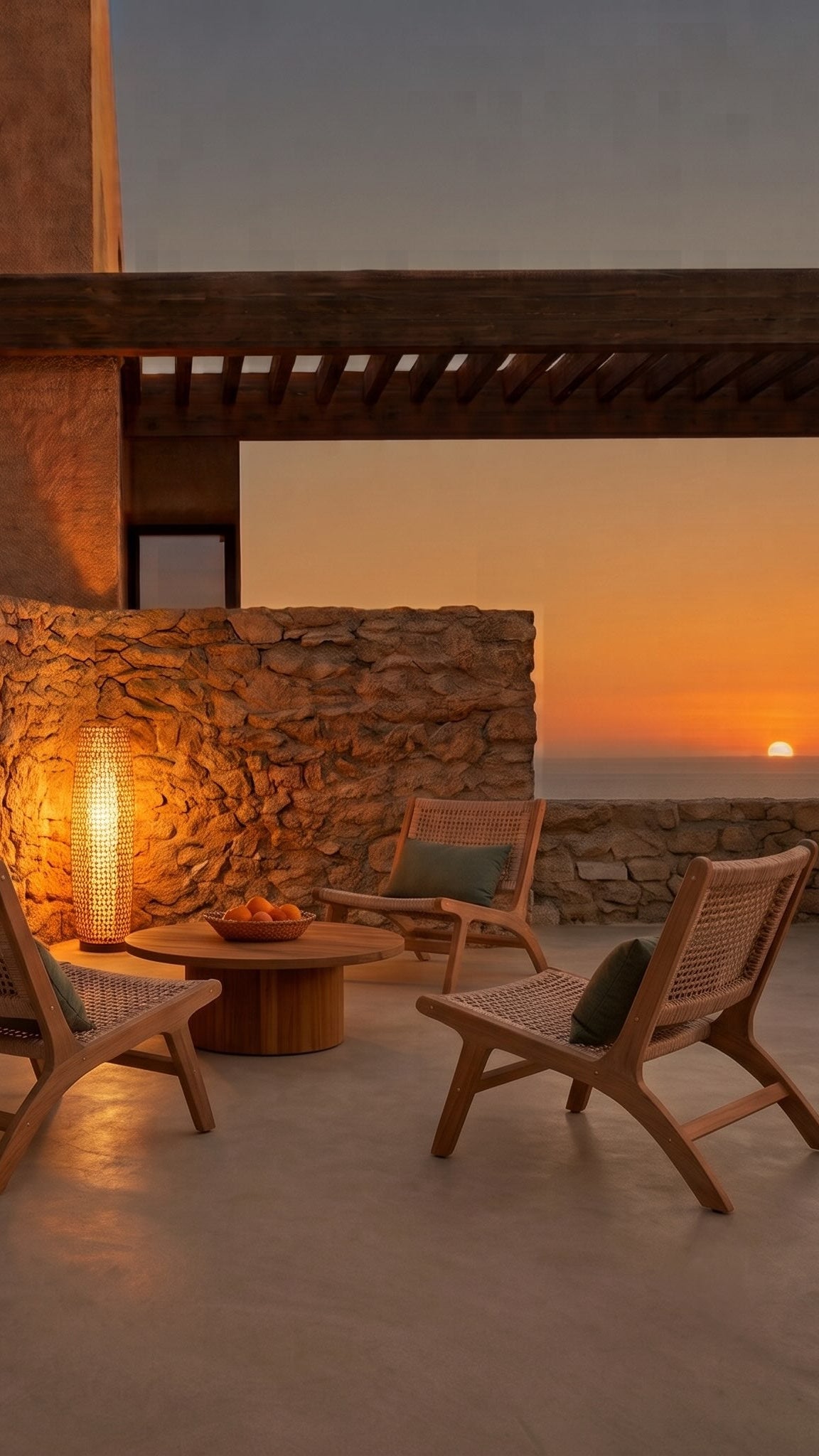 Terrasse méditerranéenne : lampadaire en rotin tressé, fauteuils cannés et mur en pierre au coucher du soleil